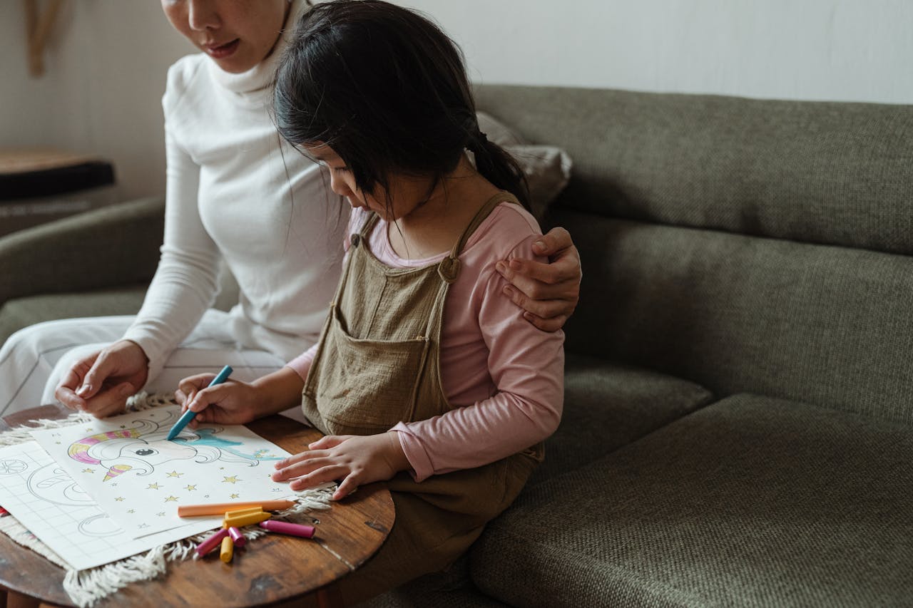 A mother helps her daughter with a colorful drawing at home, fostering creativity and bonding.